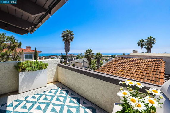 Panoramic view from a balcony showcasing a coastal area with ocean and rooftops.