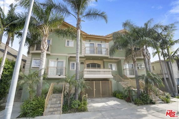 Front view of a multi-story residential building with balconies and palm trees.