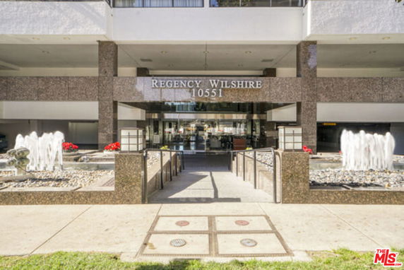 Front view of a building entrance labeled Regency Wilshire with fountains at the sides.