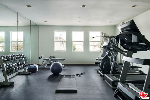 Room with gym equipment, including treadmills, dumbbells, and a yoga ball.