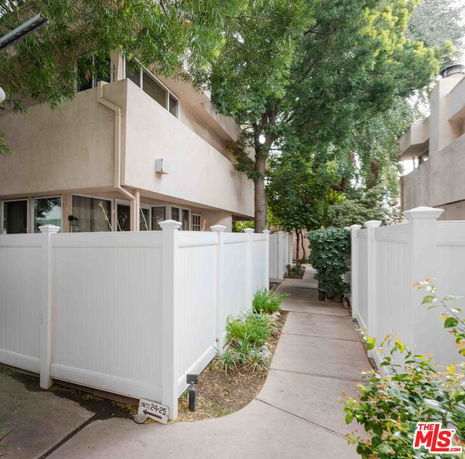 Side view of a residential building with white fencing and surrounding greenery.