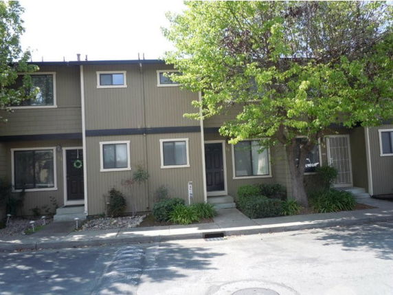 Front view of a two-story townhouse with wooden siding and small front gardens.
