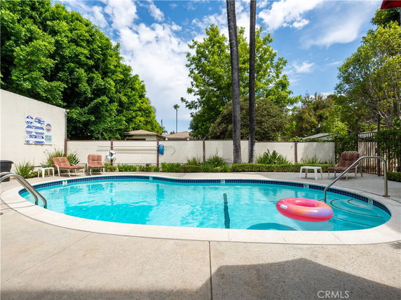 Outdoor swimming pool with surrounding trees and lounge chairs.