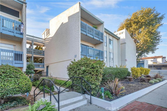 Front view of a multi-story building with balconies and landscaped entrance.