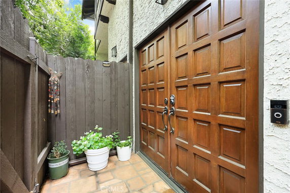 Entrance view with a wooden double door and potted plants on a tiled porch.