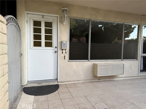 Exterior view of a building entrance with a white door, large windows, and an air conditioning unit.