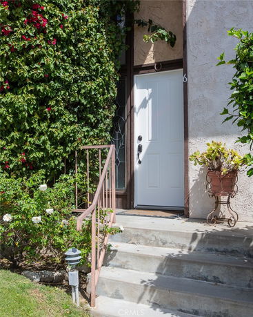 Front view of a house entrance with a white door, stairs, and surrounding vines.