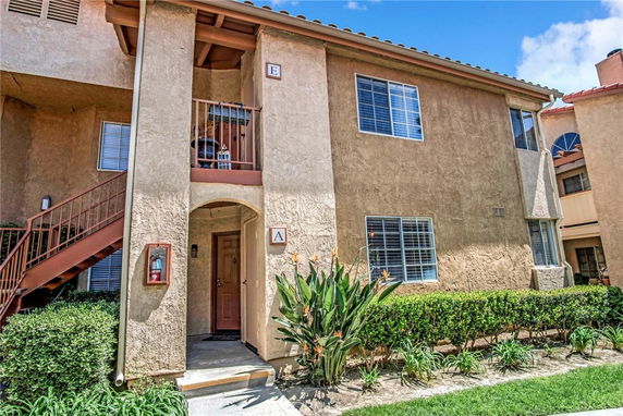 Front view of a two-story residential building with stucco exterior and a staircase leading to the upper floor.