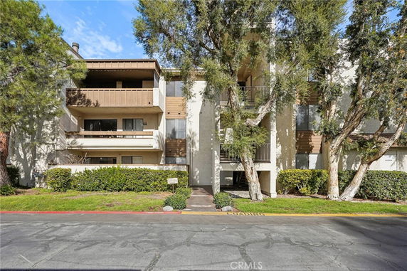 Front view of a multi-story building with balconies and trees in front.