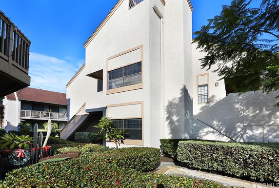 Front view of a multi-story residential building with exterior stairs and greenery.