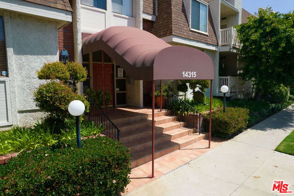 Front view of a residential building entrance with a red awning and stairs.