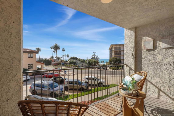 View from a balcony overlooking a street with parked cars and a distant view of the ocean.