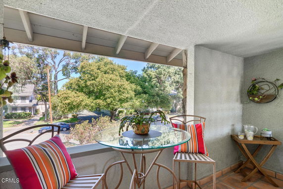 Outdoor view from a covered balcony with seating area overlooking trees and a street.