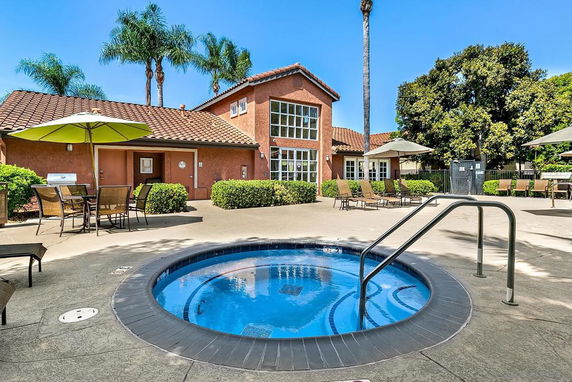 Outdoor area with a small circular pool and a two-story building with a red tile roof.