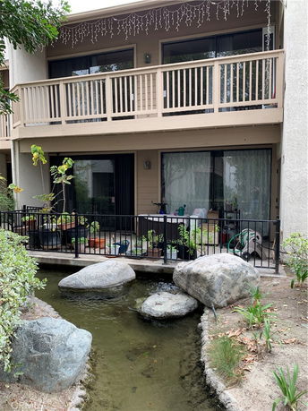 View of a multi-level building with balconies and a small artificial pond with rocks in front.