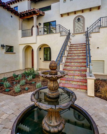 Front elevation of a multi-story house with a decorative staircase and a fountain in the foreground.