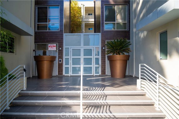 Front view of a modern building entrance with large potted plants and glass door.