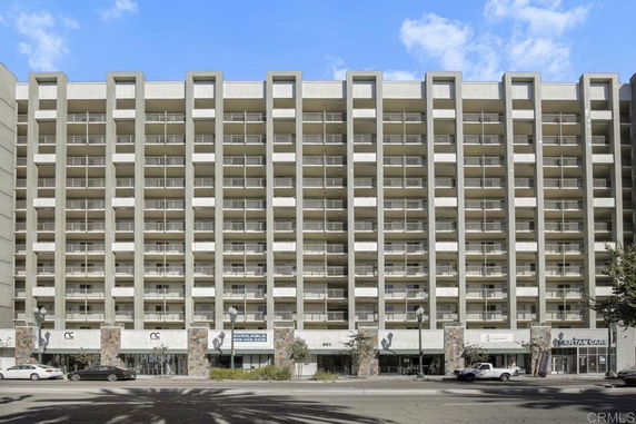 Front view of a multi-story commercial building with balconies and retail space on the ground floor.