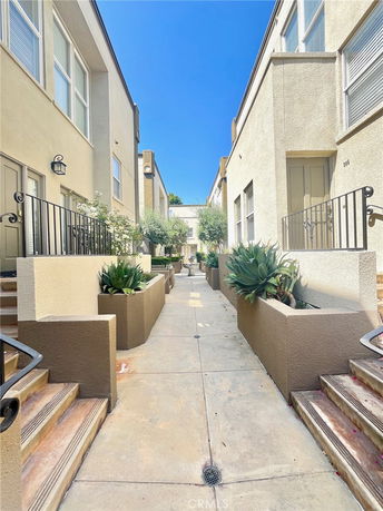 Front view of a building walkway with potted plants and stairs leading to doorways on both sides.