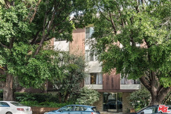 Front view of a multi-story residential building partially obscured by trees.