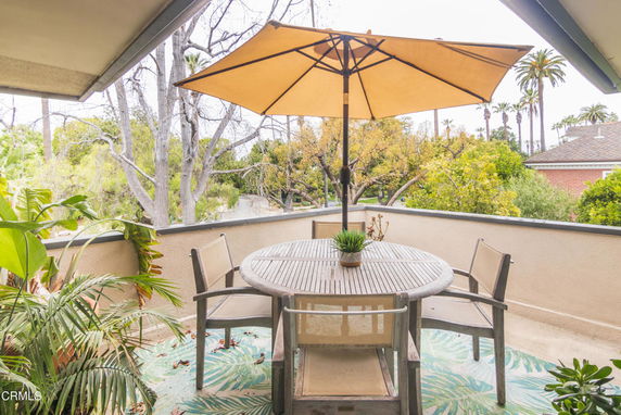 Outdoor patio area with a round table and umbrella, surrounded by trees.