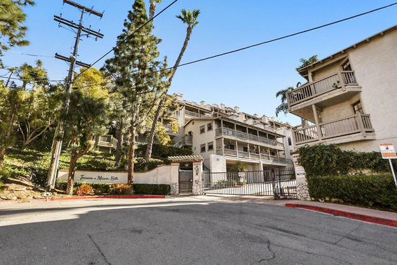 Front view of multi-story apartment building with balconies and gated entrance.