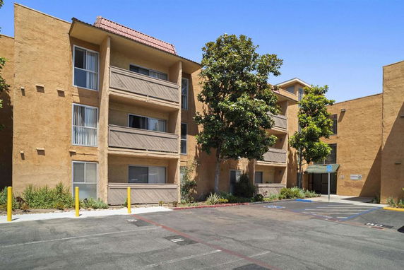Front view of a three-story apartment building with balconies and parking area.