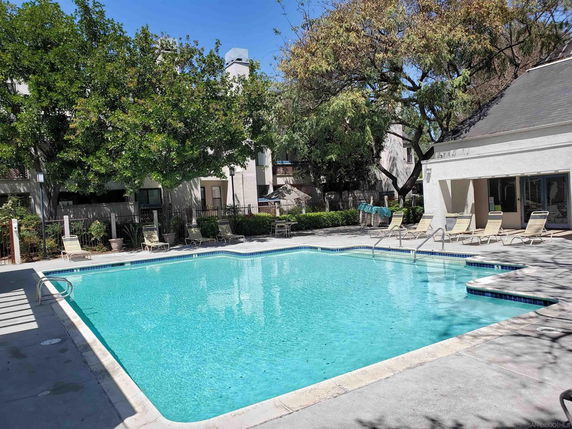 Outdoor swimming pool area with lounge chairs and greenery.