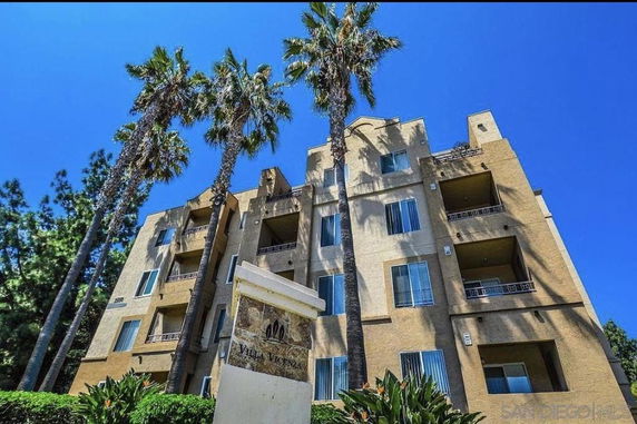 Front view of a multi-story apartment building with balconies and tall palm trees.
