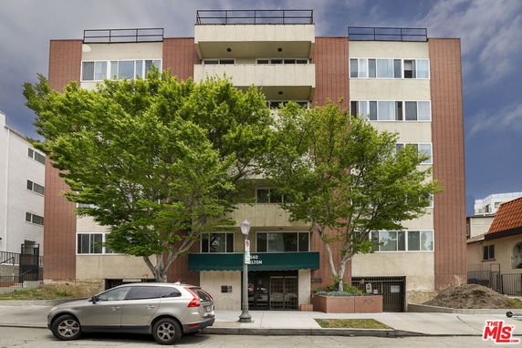 Front view of a multi-story building with trees and a parked car.