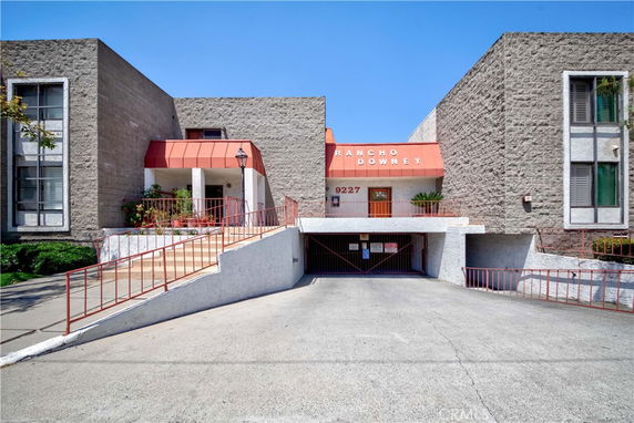 Front view of a building with a red canopy entrance and a gated parking area below.
