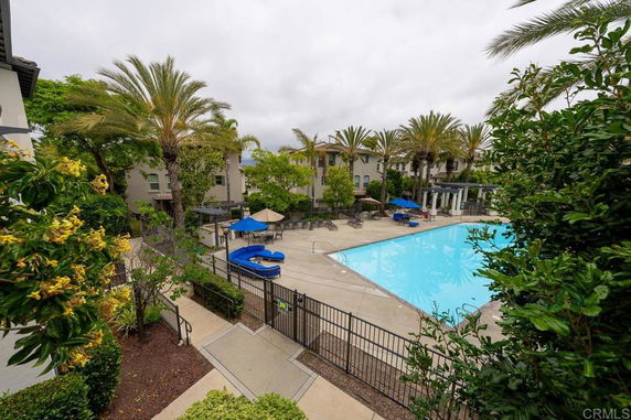 Outdoor swimming pool area with surrounding greenery and buildings.