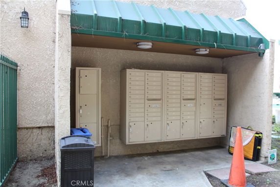 Outdoor area with multiple mailboxes mounted on a wall under a green awning.