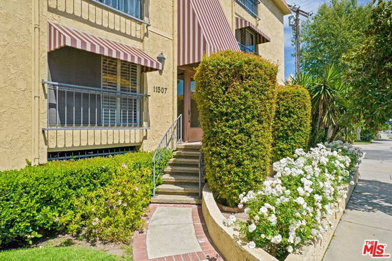 Front view of a residential building with striped awnings and steps leading to the entrance.