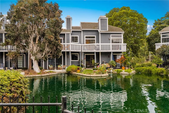 Front view of a two-story house with a balcony and adjacent pond.