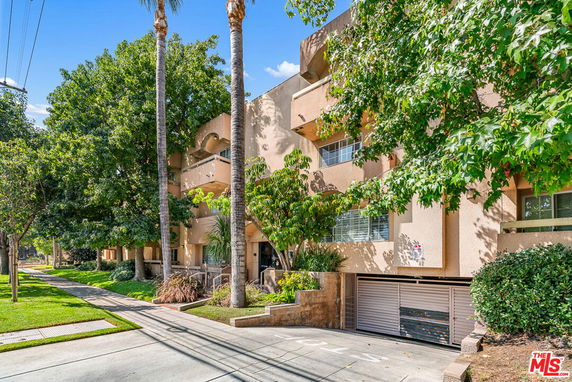 Front view of a multi-story residential building with balconies and surrounding trees.