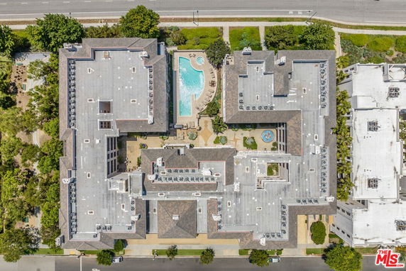 Aerial view of a large residential building with a central swimming pool and surrounding green areas.