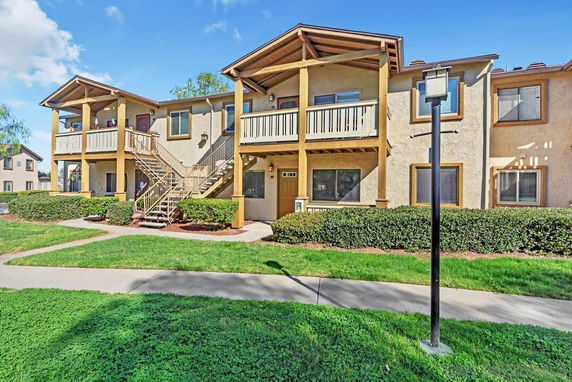 Front view of a two-story residential building with wooden balconies and outdoor stairs.