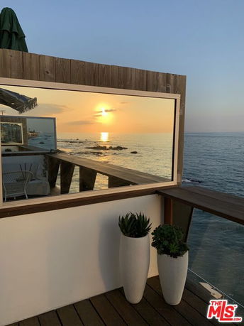 Deck area with ocean view at sunset seen through large window.