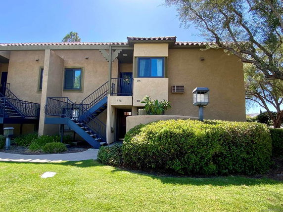 Front view of a two-story building with stairs leading to upper units and a small garden area.