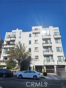 Front view of a multi-story residential building with balconies and a palm tree in front.