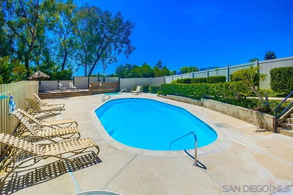 Outdoor swimming pool with surrounding lounge chairs and privacy fencing.