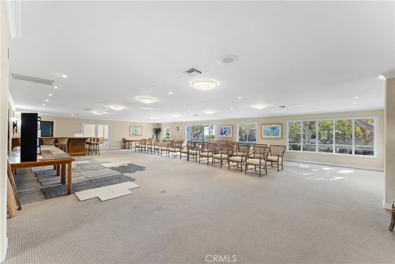 Spacious clubhouse room with seating, large windows, and ceiling lights.