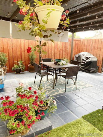 Outdoor patio area with a table, chairs, potted plants, and a barbecue grill, under a pergola.