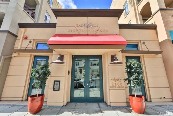 Front view of a commercial-style building with red awning and potted plants.