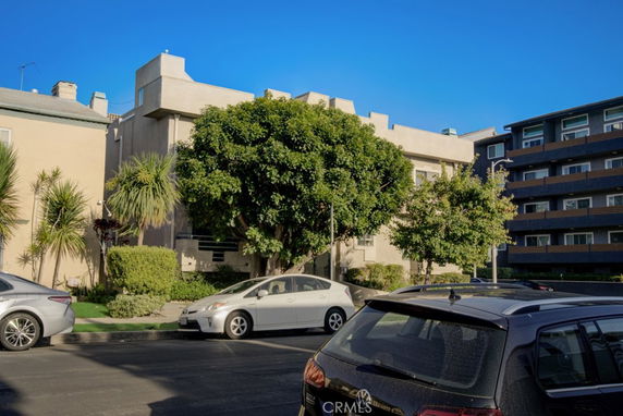 Front view of a multi-story building with surrounding trees and parked cars.