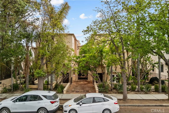 Front view of a multi-story residential building with trees in front and parked cars on the street.