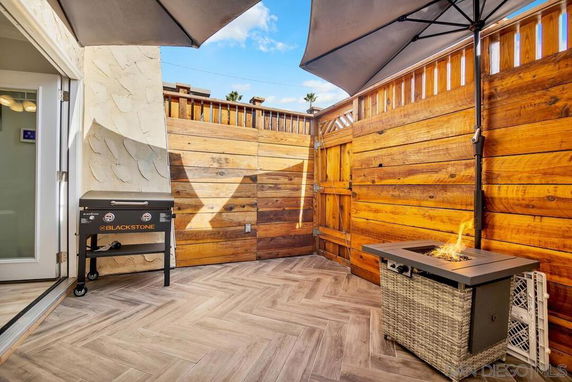 Outdoor patio area with a wooden privacy fence, a Blackstone grill, and a fire pit under large patio umbrellas.