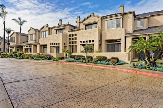 Front view of a row of two-story townhouses with beige exterior and plants lining the entrance.
