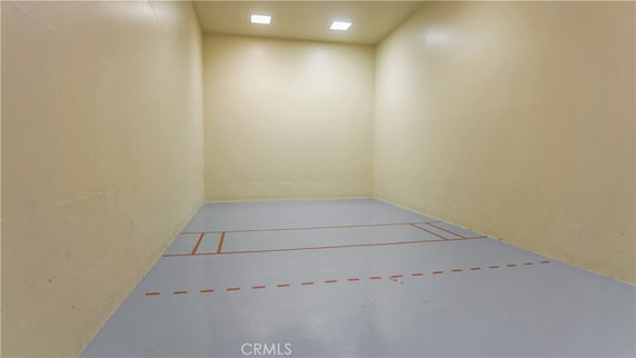 Indoor squash court with light-colored walls and markings on the floor.